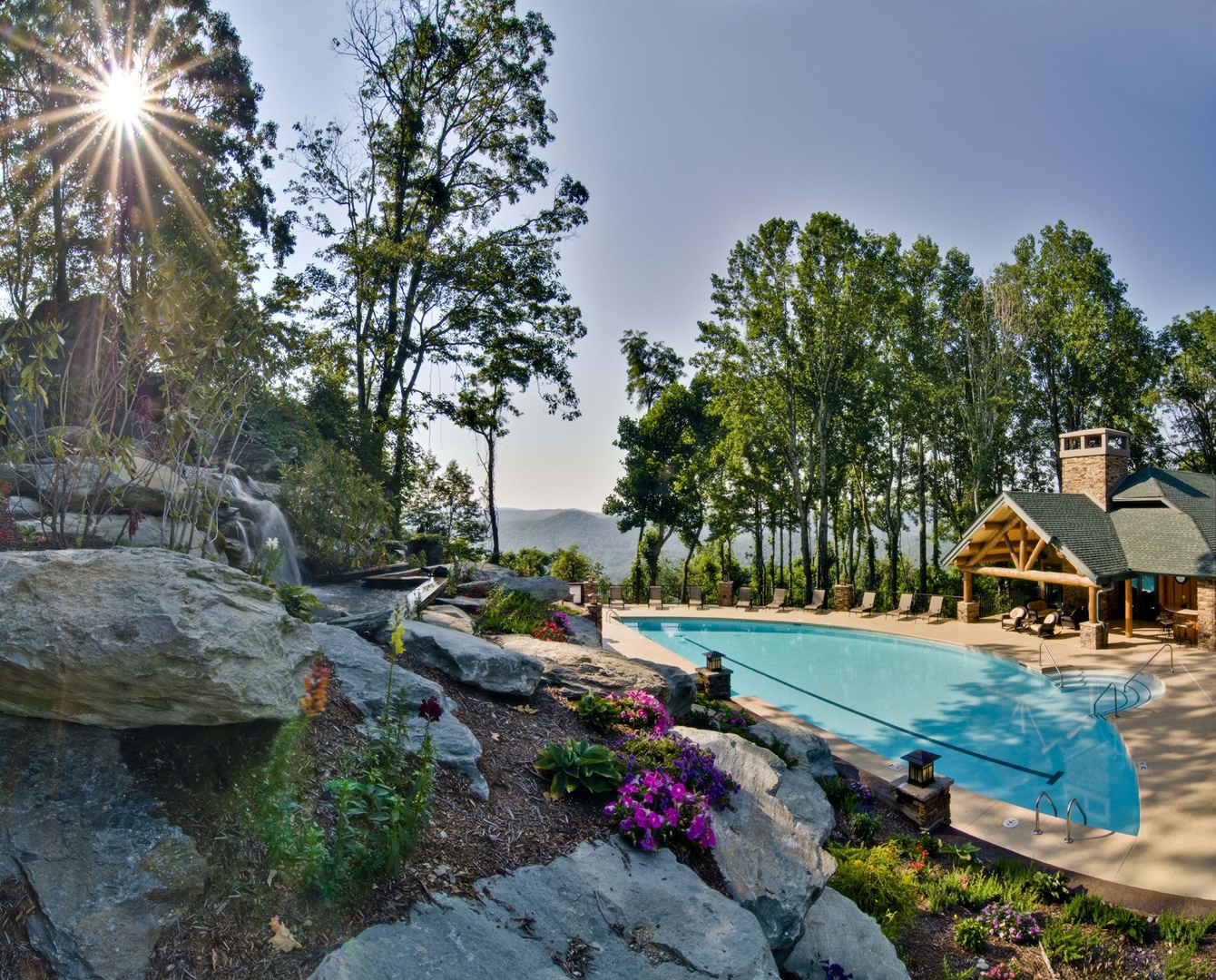 Stunning mountain views frame the expansive pool area, where natural rock formations blend into manicured gardens. The pavilion offers shaded relaxation amid the peaceful, tree-lined setting.