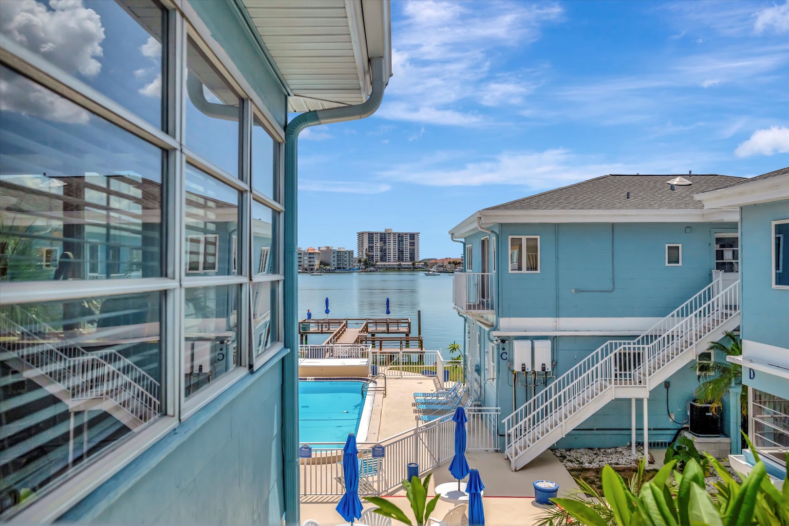 Coastal property featuring pool access, private dock with bay views, and waterfront grounds under sunny skies.