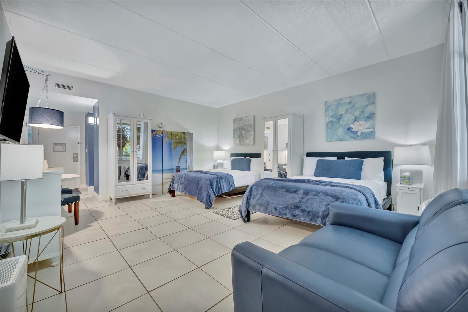 Your spacious beach-style suite features two plush queen beds, a cozy seating area, and tile floors that stay cool underfoot. Enjoy the calming coastal palette and modern comforts—your perfect home away from home.