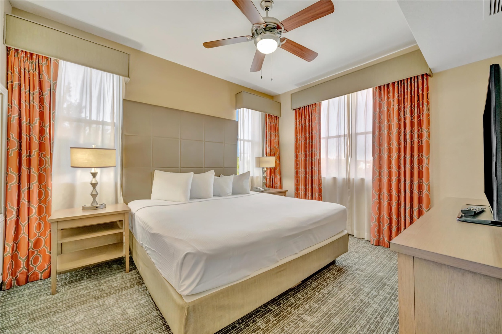 Sink into crisp white linens and let your worries drift away as the ceiling fan hums overhead, while warm natural light filters through elegant curtains to brighten your restful sanctuary.