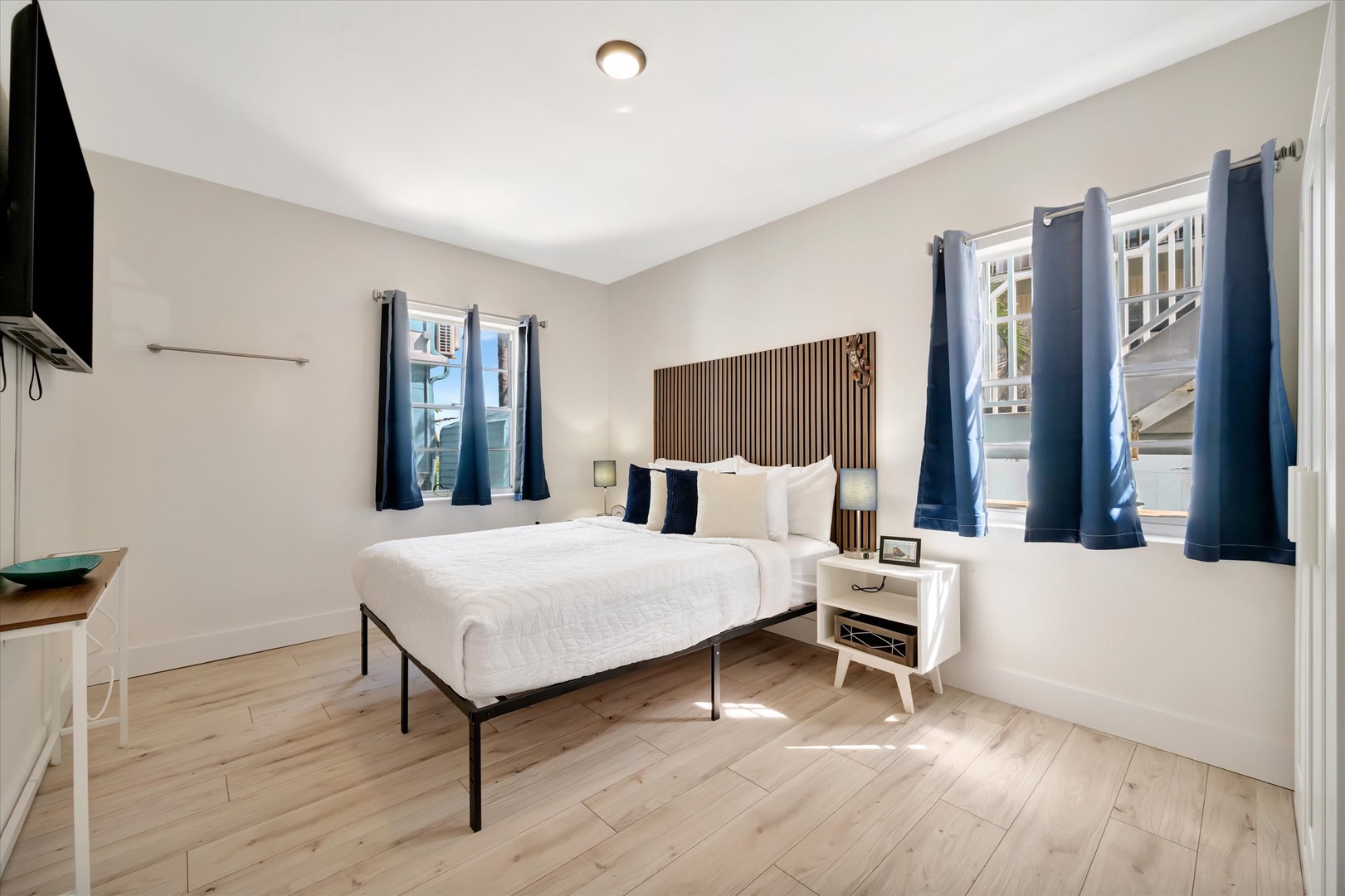 Step into your serene retreat—a bright, airy bedroom with crisp white linens, warm wood floors, and natural light pouring through picture-perfect windows. Unwind in this calming space where modern comfort meets coastal charm.