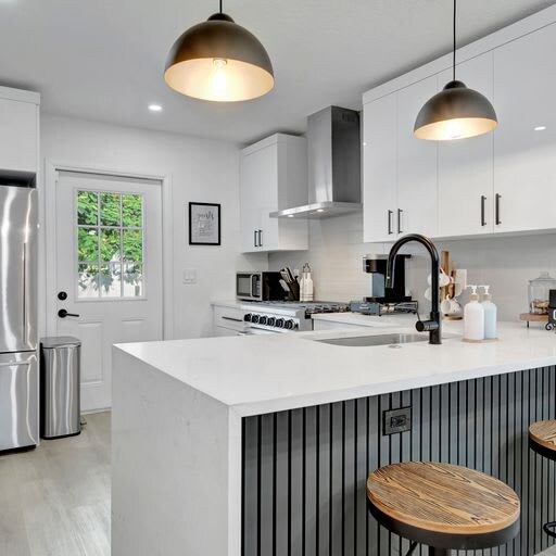 Step into your modern chef's kitchen with sleek white countertops, stainless steel appliances, and warm pendant lighting overhead. The spacious island invites you to gather, cook, and create memories in this bright, thoughtfully designed space.