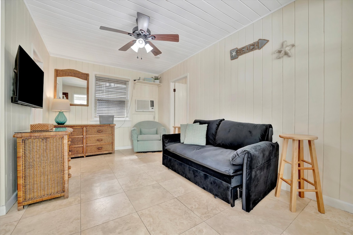 Step into your cozy coastal retreat, where cottage charm meets comfort. Unwind on the plush sofa, feel the ceiling fan's breeze, and let the beachy vibes wash over you.
