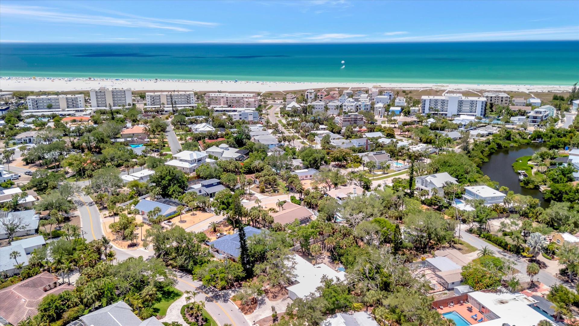 Aerial view of a coastal residential neighborhood with pristine white sand beaches and emerald waters just steps away, offering easy access to beachfront living.