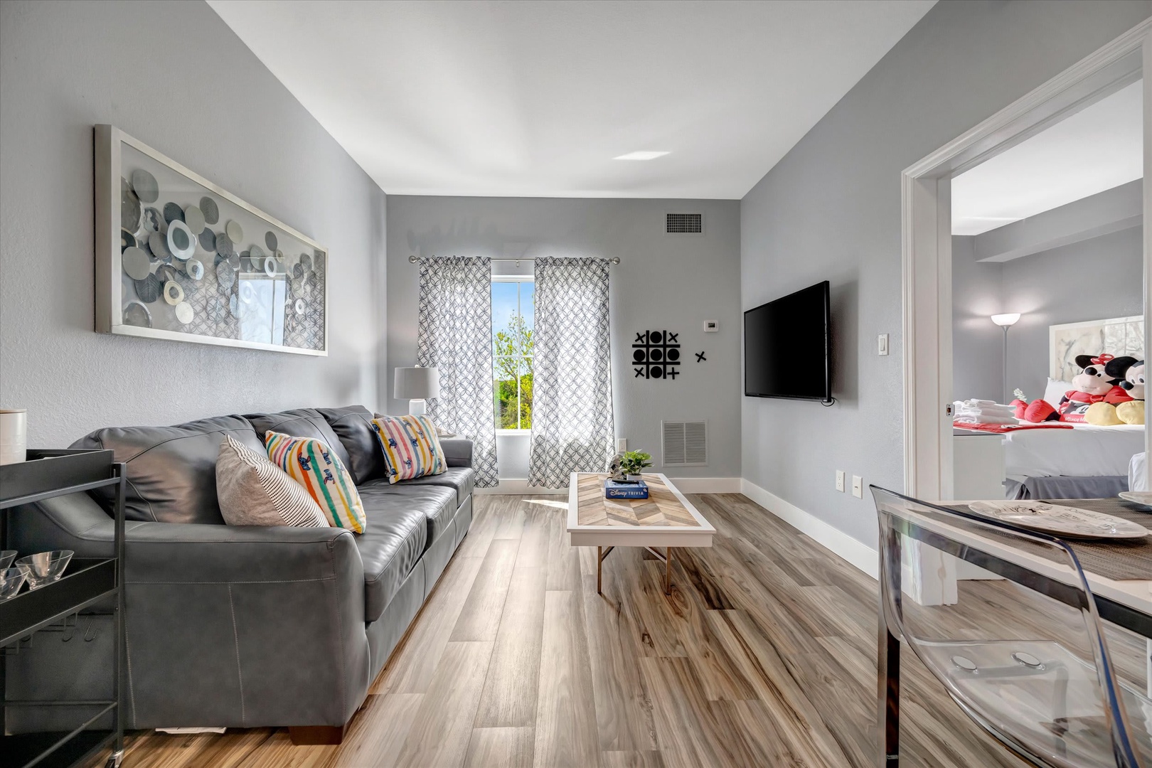 Sink into the plush leather sofa and enjoy your favorite shows in this bright, modern living space with natural light streaming through patterned curtains and stylish decor throughout.