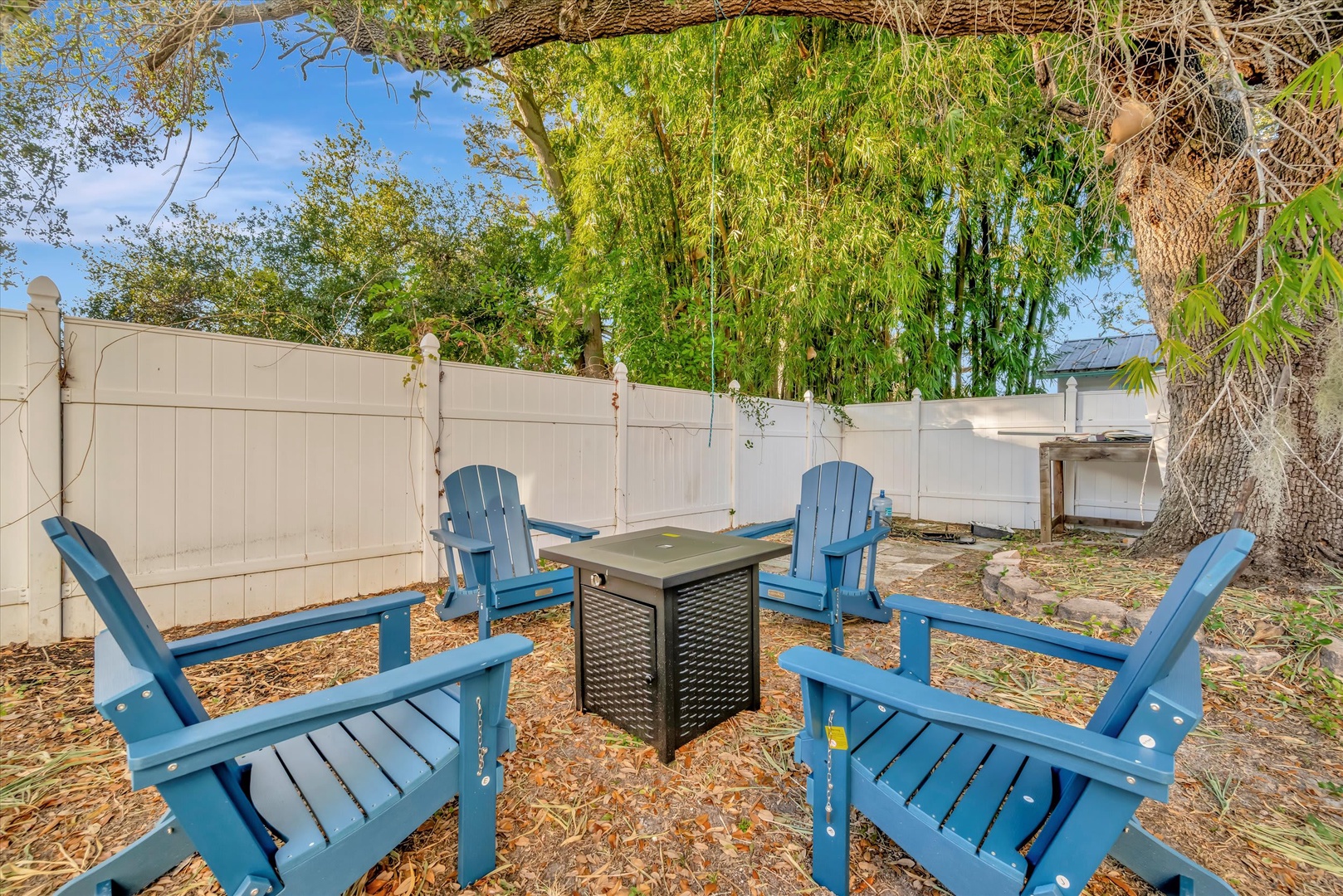 Your own private retreat awaits under the shade of a graceful willow, where blue Adirondack chairs circle a cozy fire table—perfect for evening conversations or morning coffee in complete privacy.