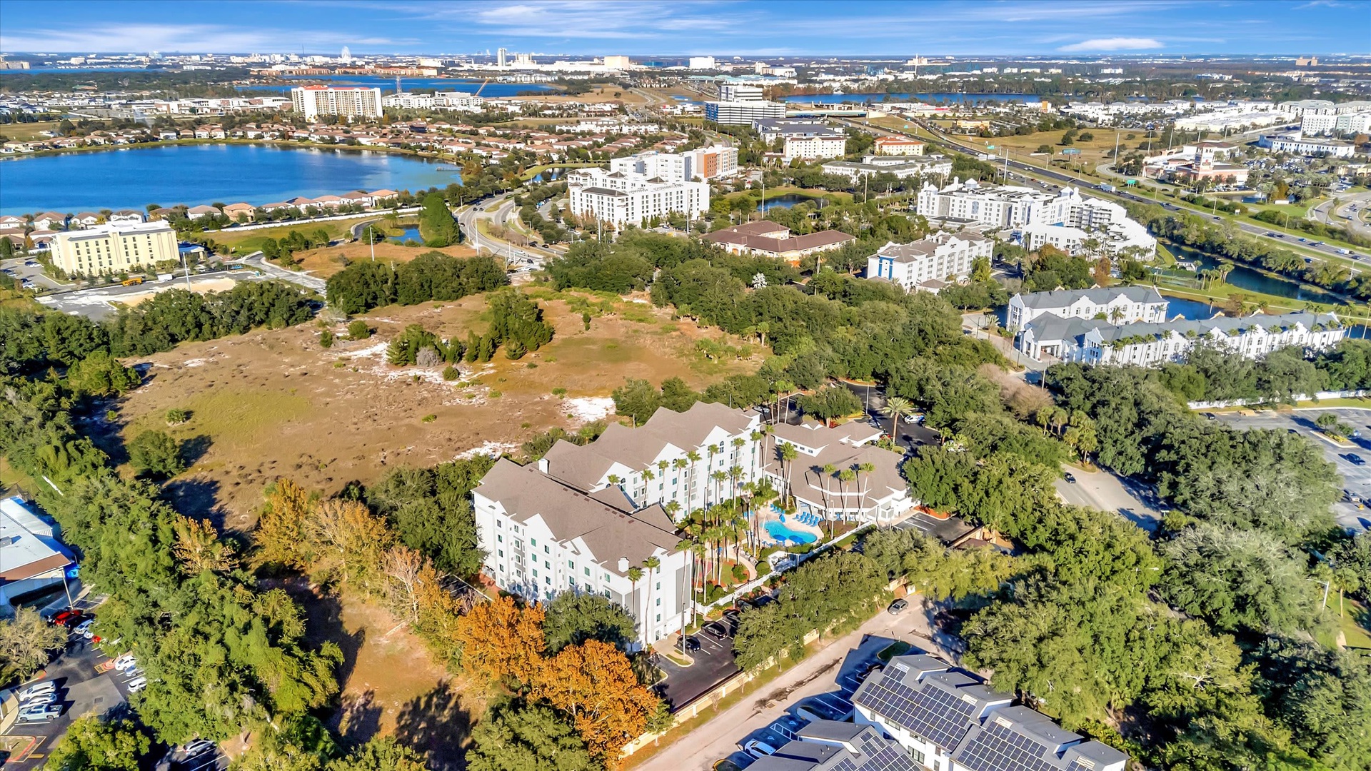 Aerial view of the property nestled in lush greenery with a sparkling pool at its center, surrounded by residential neighborhoods, waterways, and abundant natural landscape.