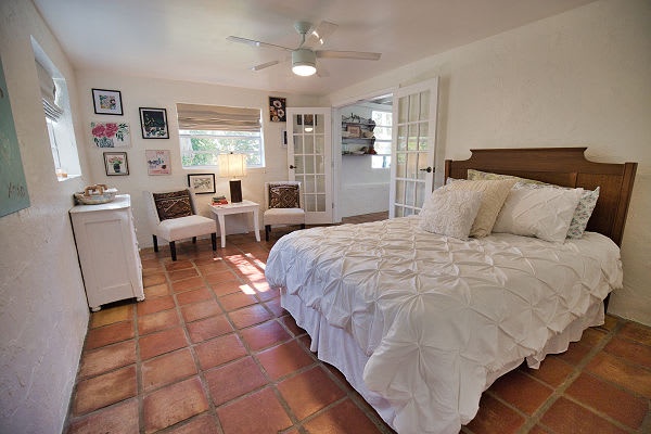 Step into your bright retreat with terracotta tile floors, a plush bed, and a cozy seating nook—your peaceful home away from home awaits.