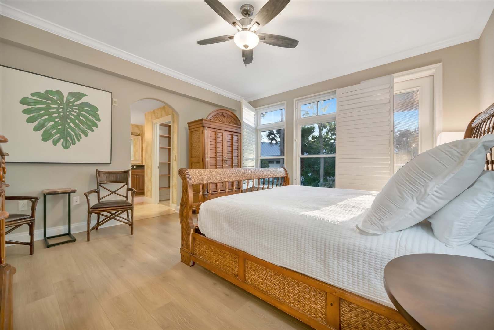 Serene coastal bedroom with natural light, plush king bed, tropical decor, and ceiling fan for the perfect retreat.