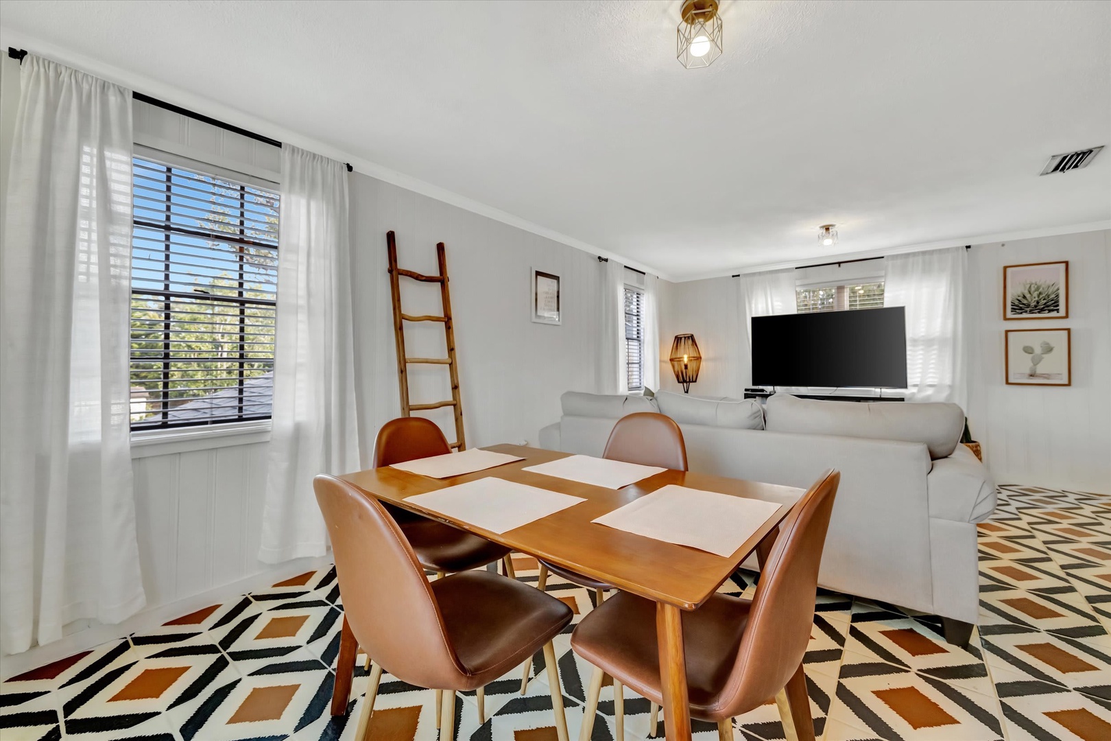 Gather around the stylish dining table where bold geometric floors and natural light through plantation shutters create an inviting backdrop for your meals and conversations.