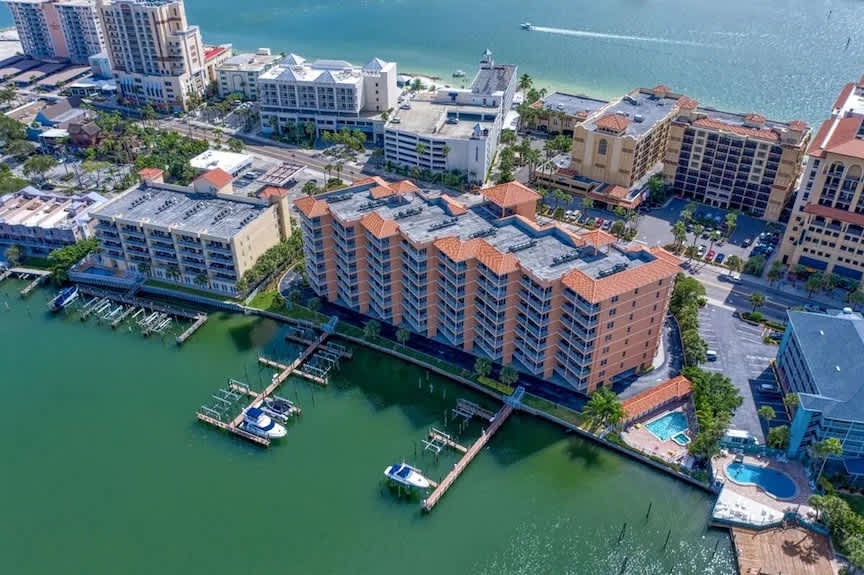 Aerial view of a waterfront resort complex featuring marina docks, swimming pools, and multi-story buildings nestled along the bay's edge.