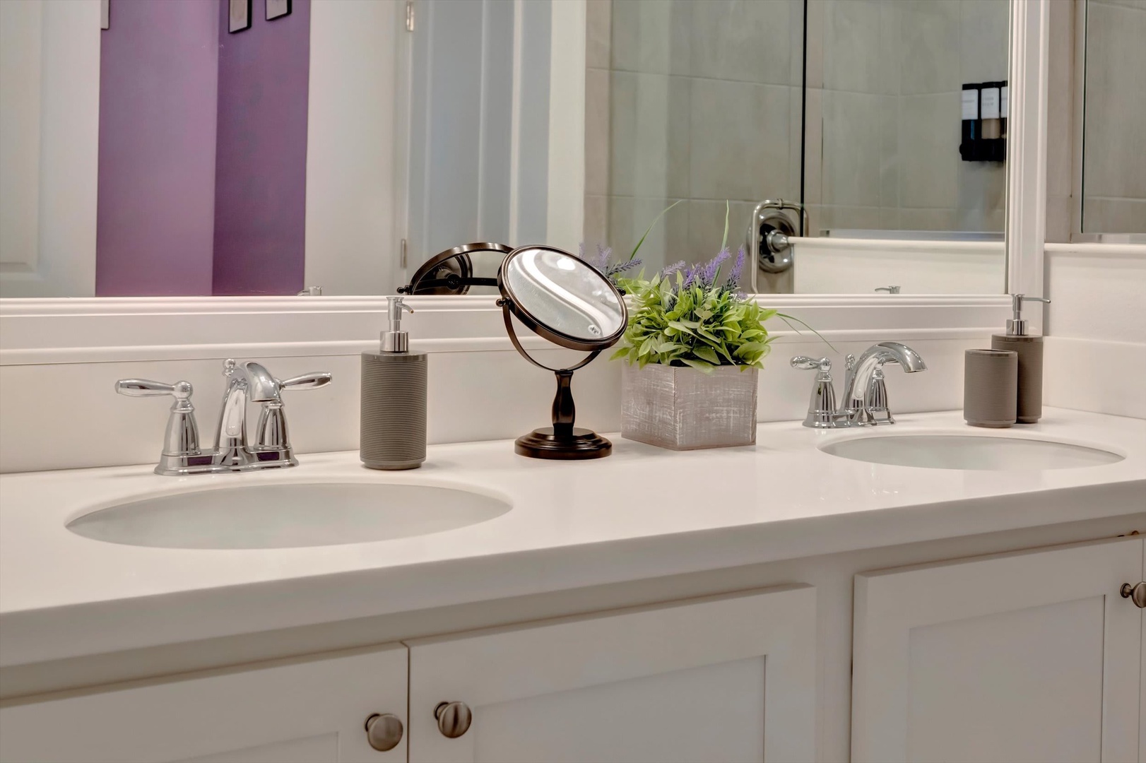 Freshen up at your private dual-sink vanity, thoughtfully styled with a magnifying mirror and soft lavender accents visible through the mirror—a calming retreat.