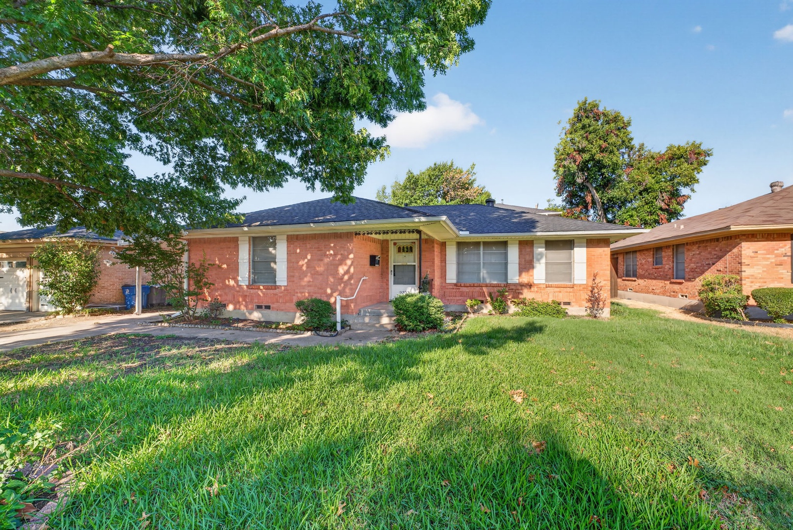 A charming single-story brick home nestled in a peaceful residential neighborhood, surrounded by mature trees and a welcoming front yard.