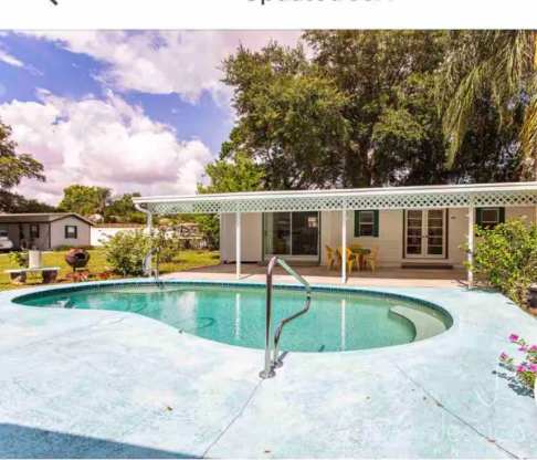 The property features a sparkling outdoor pool surrounded by a spacious patio area, shaded by mature trees and adjacent to a covered terrace with patio furniture—perfect for sunny days and warm evenings.