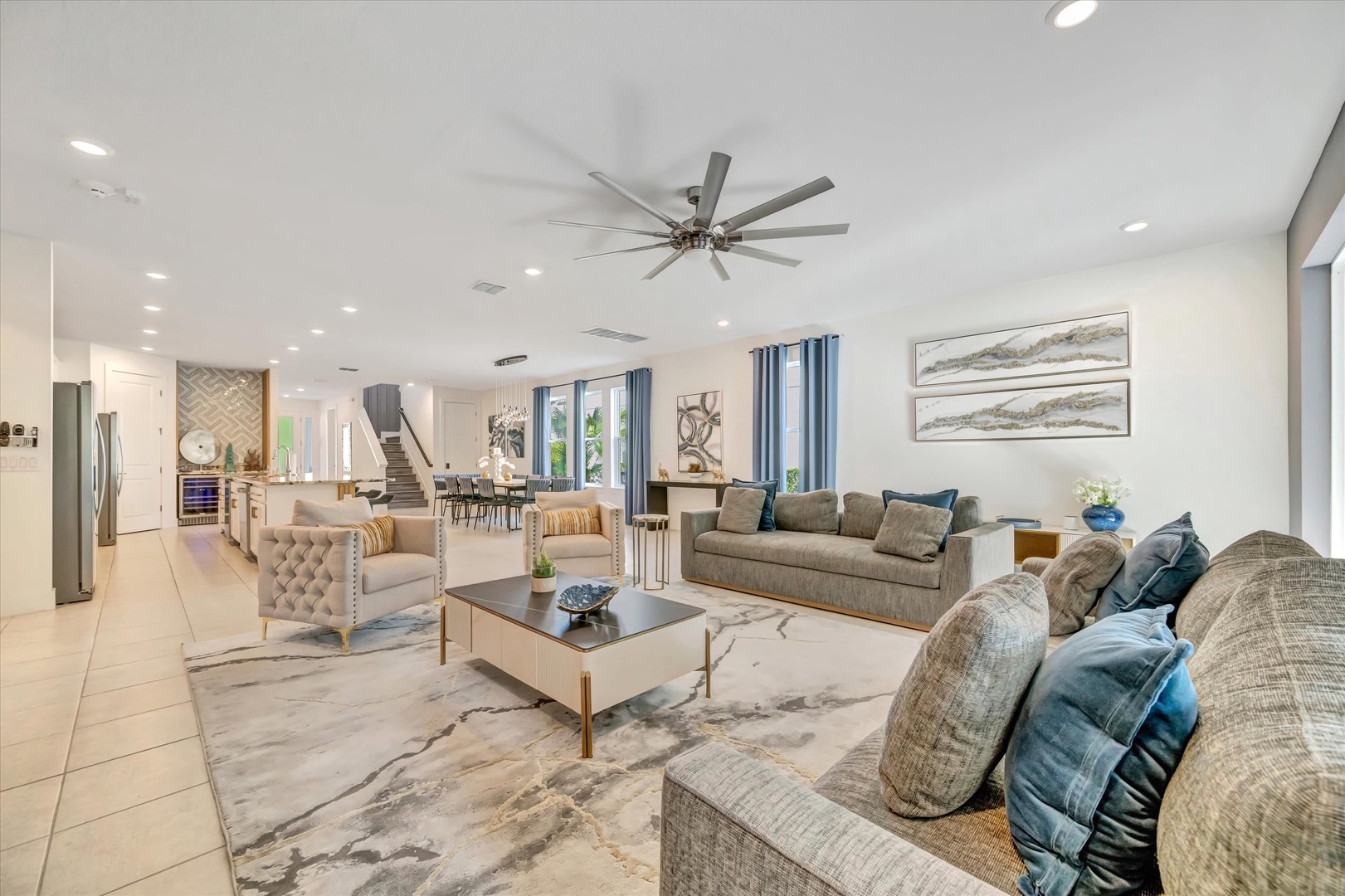 Step into your spacious living room where soft textures and coastal hues create a serene retreat. High ceilings and natural light invite you to unwind on plush seating while staying cool under modern ceiling fans.