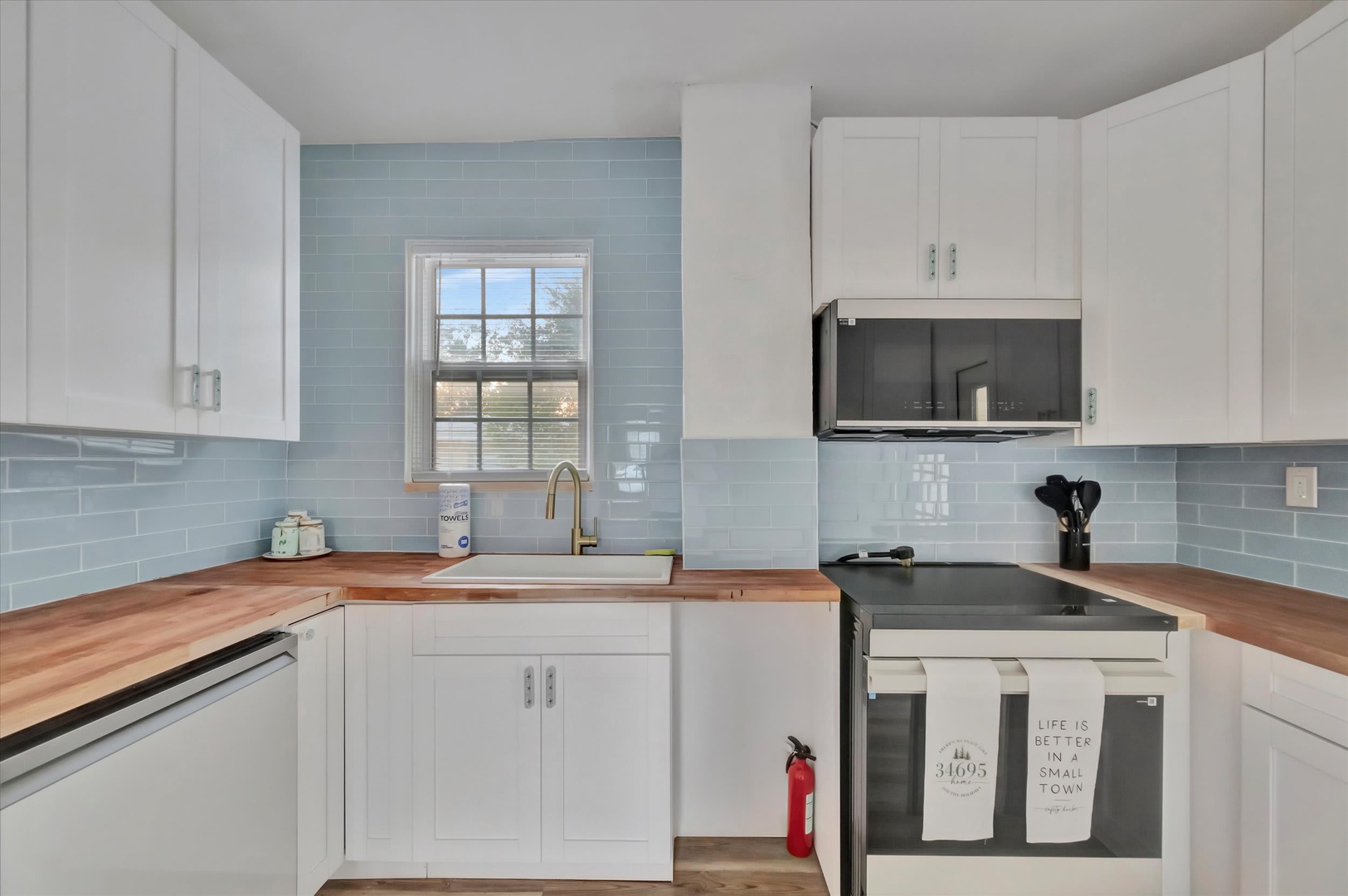 Whip up your favorite meals in this bright, modern kitchen with warm butcher-block counters, sleek white cabinetry, and soothing blue subway tile that brings a touch of coastal charm.
