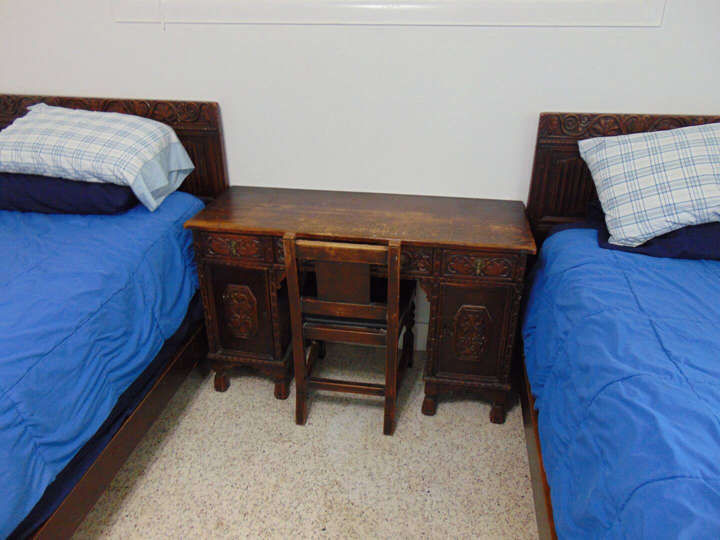 Twin beds with cheerful blue linens flank an ornate wooden desk, creating a cozy guest room where you can unwind after exploring the area.