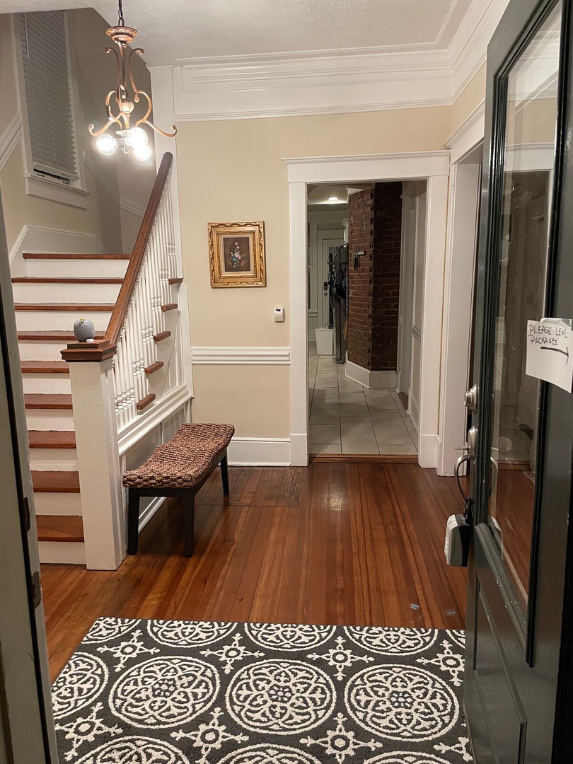 Step into your welcoming entryway, where polished hardwood floors and classic architectural details set the tone for your entire stay. The warm chandelier and charming staircase invite you to settle in and feel at home.