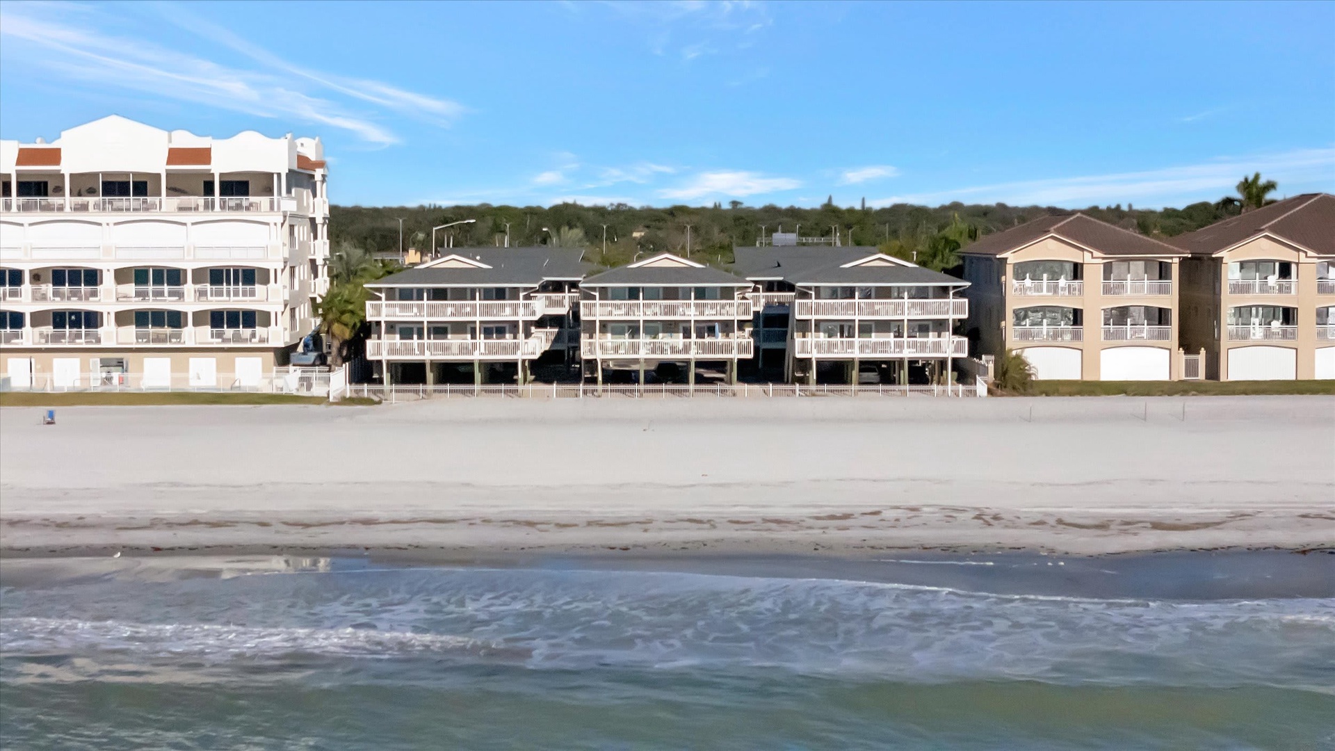 Beachfront vacation rental complex offering direct access to a wide sandy shore and gentle surf, with private balconies facing the ocean.