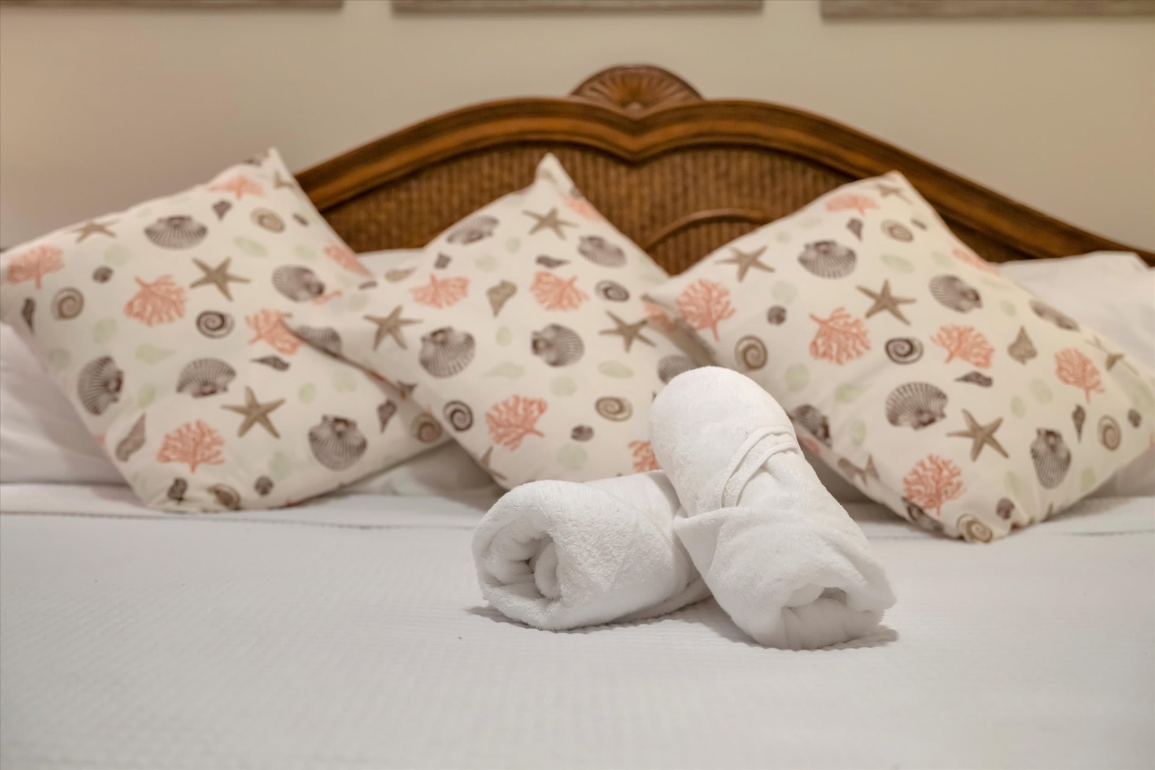 Your coastal-themed bedroom awaits with crisp linens, charming seashell-patterned pillows, and fluffy towels arranged with care—everything ready for your relaxing beach getaway.