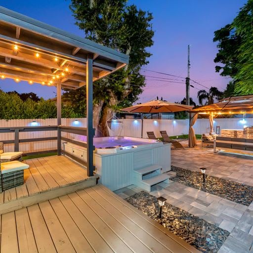 An inviting backyard retreat awaits, where warm string lights illuminate a private hot tub and poolside lounge area—your perfect spot to unwind under the evening sky.