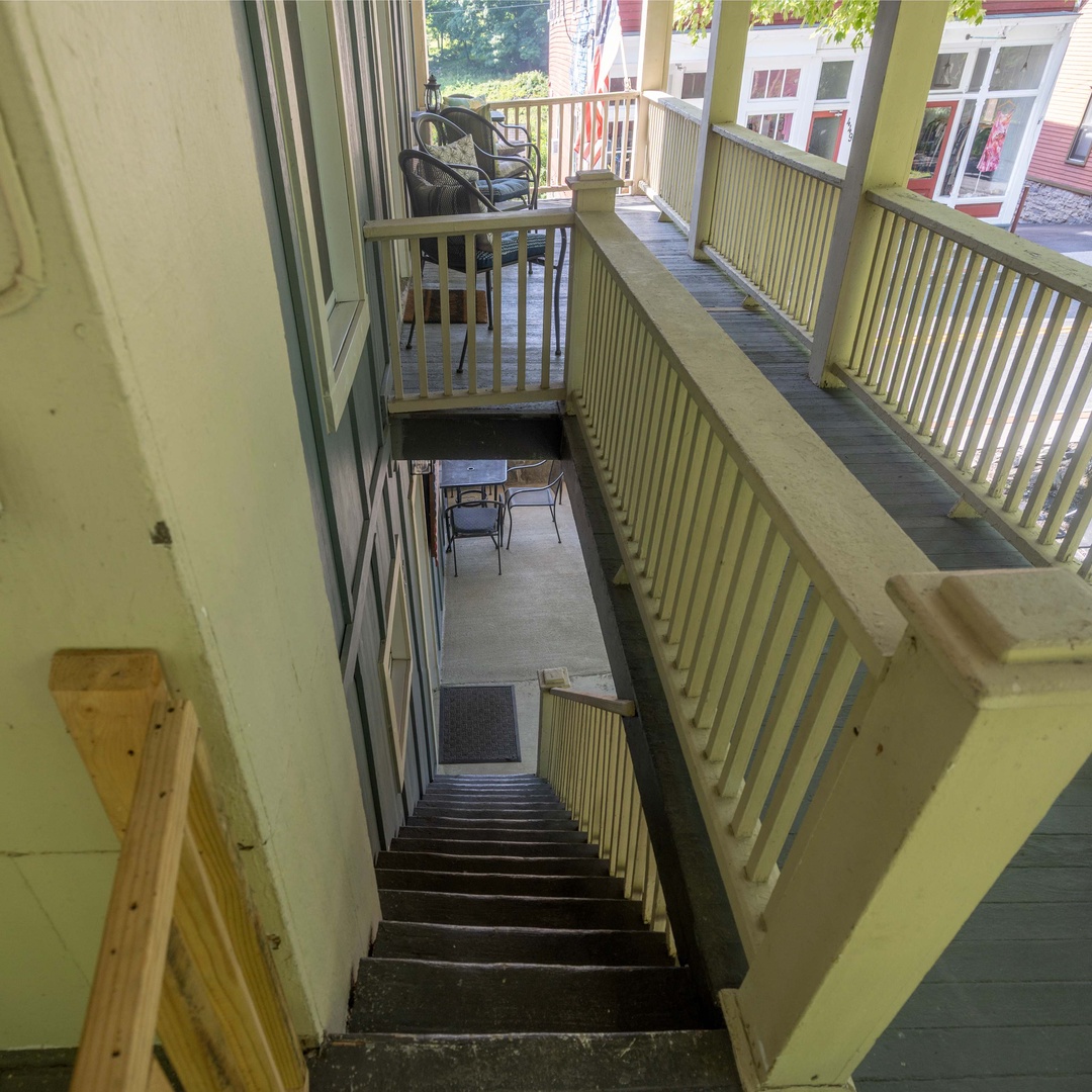 Multi-level staircase and outdoor balcony seating areas overlook a charming neighborhood street with local shops and greenery.