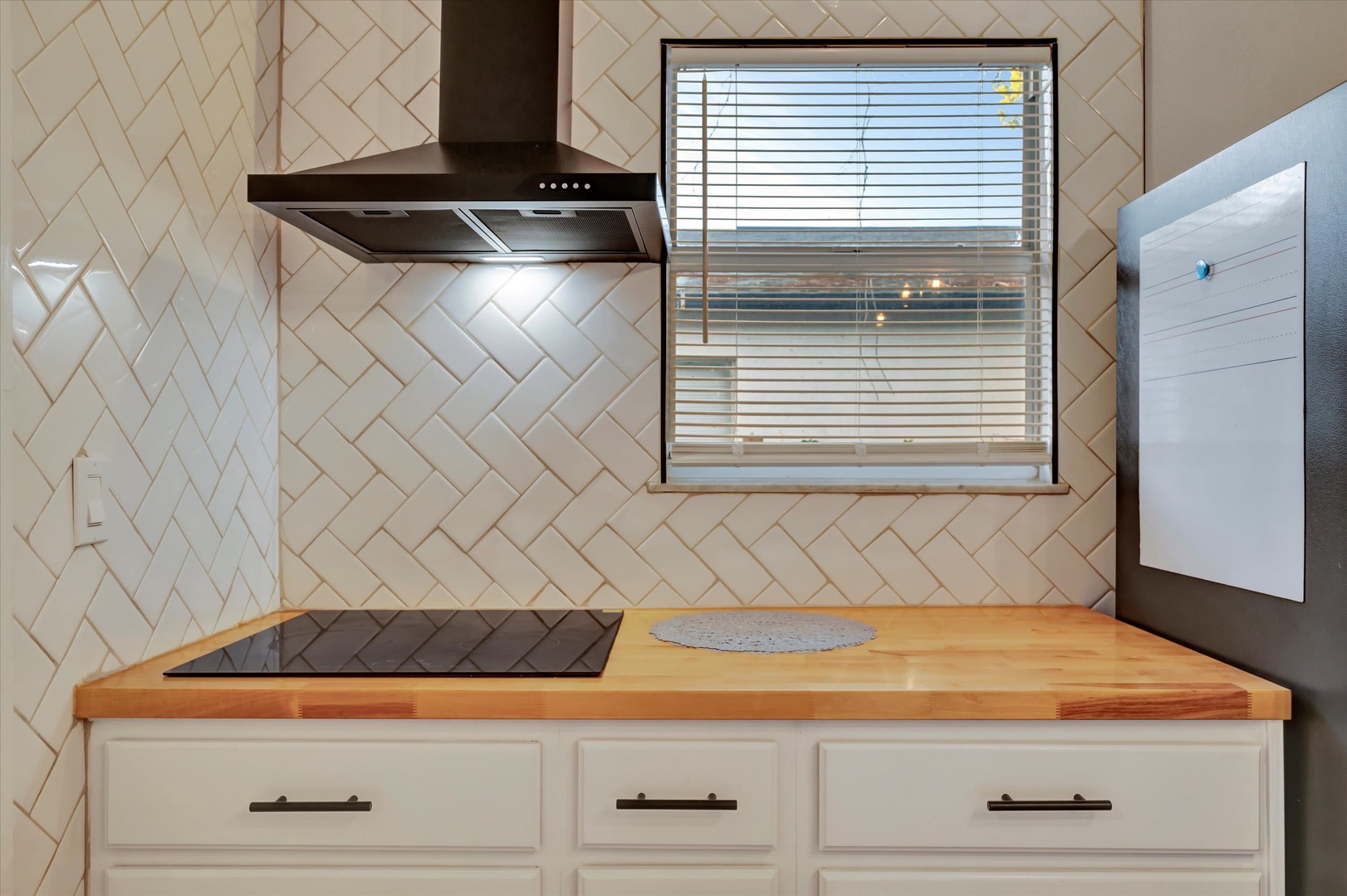Your modern kitchen awaits with sleek appliances and butcher block countertops, ready for meal preparation. Natural light filters through the window, illuminating the elegant herringbone tile backsplash.