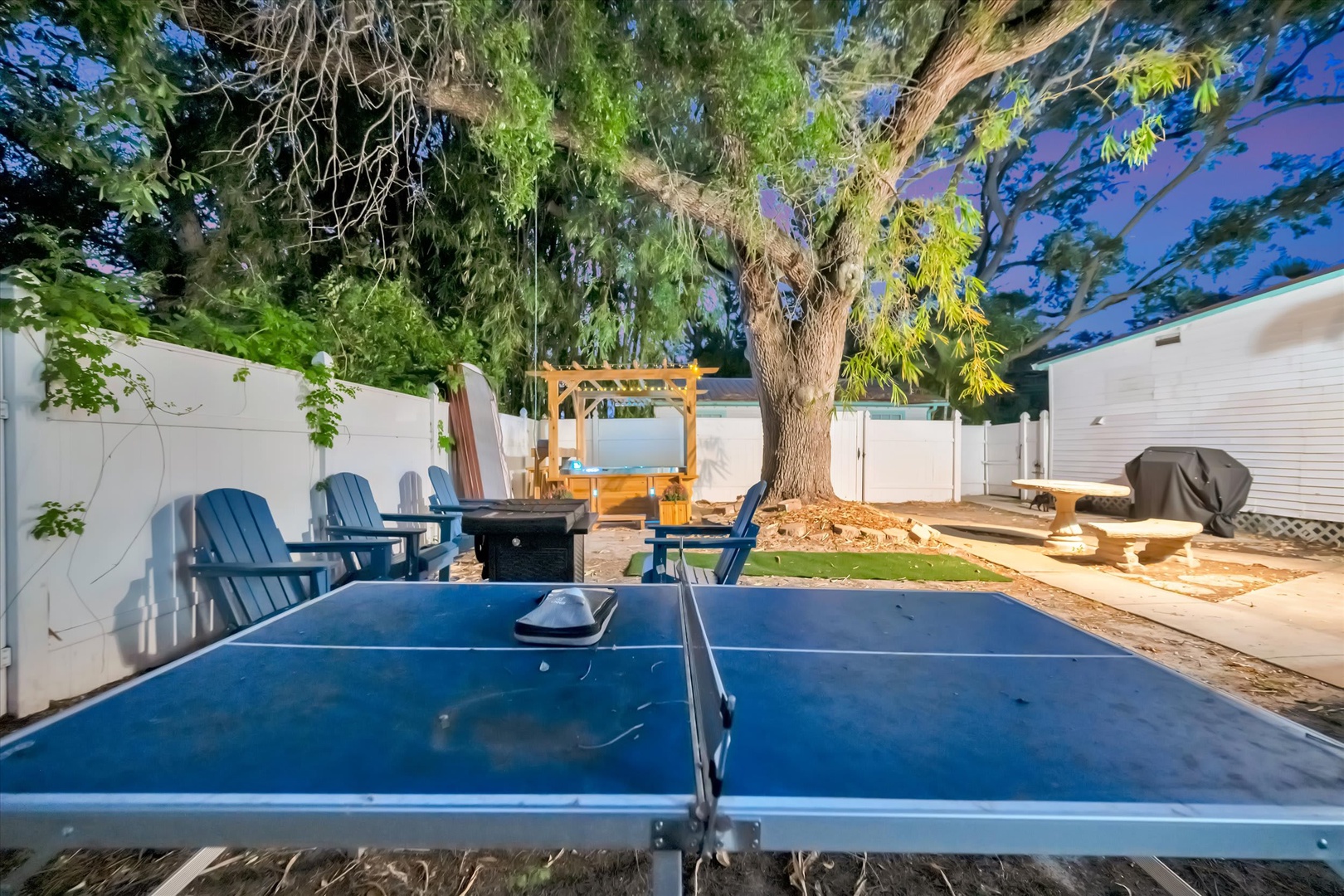 Your private backyard oasis awaits, featuring a ping-pong table, Adirondack chairs around a fire pit, and a shaded pergola—perfect for afternoon games and evening gatherings under the stars.