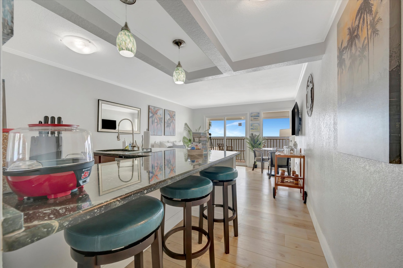 Step into your bright, open-concept kitchen and living space, where beamed ceilings and pendant lights set a welcoming coastal vibe. Gather at the breakfast bar or unwind in the airy living area that flows onto your private balcony.