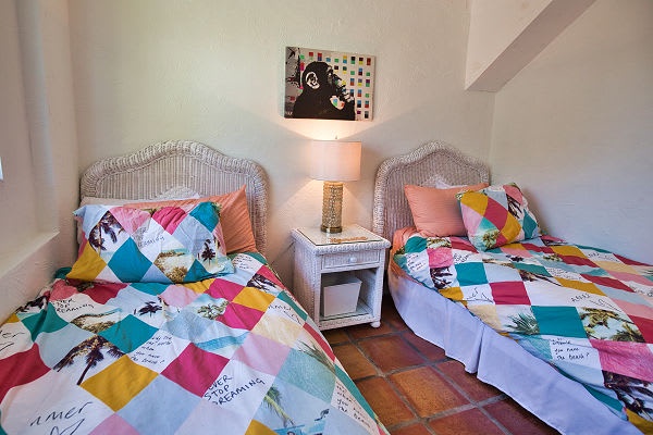 Your comfortable twin bedroom awaits with charming wicker headboards, colorful quilts, and warm terracotta tile floors that give the space a cheerful, inviting feel.
