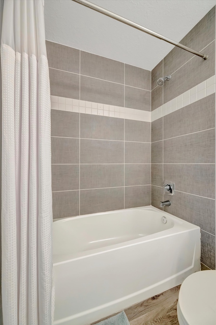 Your private bathroom features a sleek tub-shower combo with contemporary gray and white tile accents, inviting you to refresh after a day of exploring.