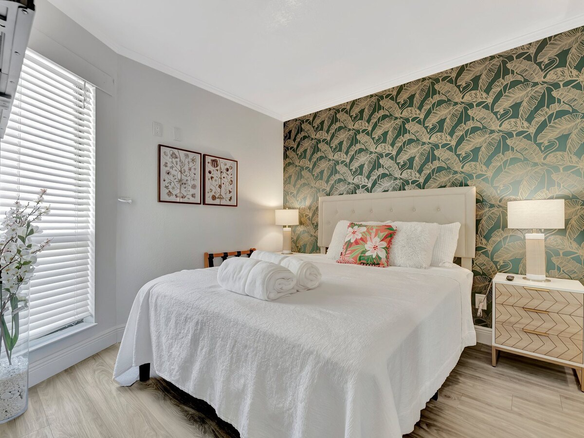 Drift off in your serene retreat, where tropical palm wallpaper and crisp linens create a calming oasis. Fresh towels await, and soft lamplight sets the perfect mood for rest.