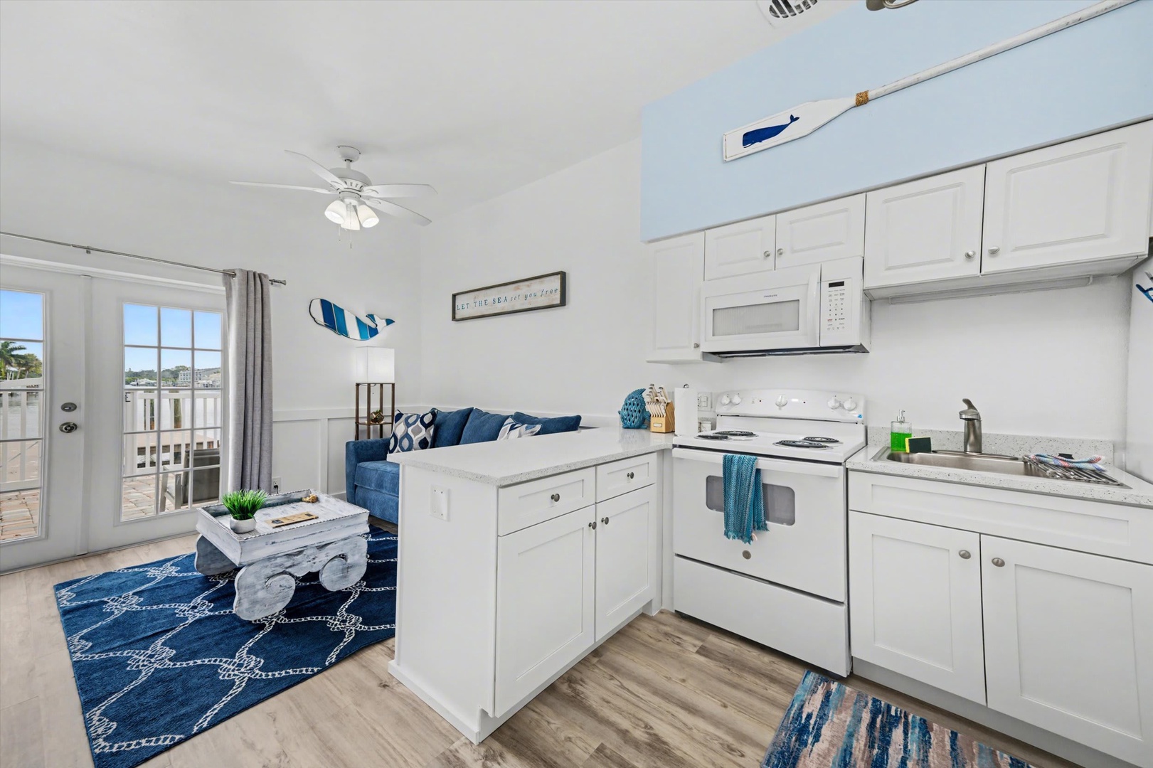 Step into your bright coastal retreat where beach-inspired blues meet crisp white throughout an open living space that flows seamlessly from kitchen to living area, with a private patio just beyond your door.