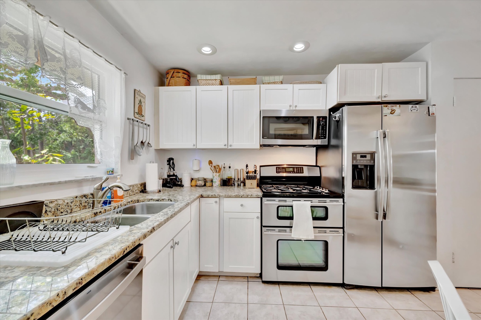 Your fully equipped kitchen features stainless appliances and granite countertops, with bright natural light streaming through crisp white curtains—perfect for preparing home-cooked meals during your stay.