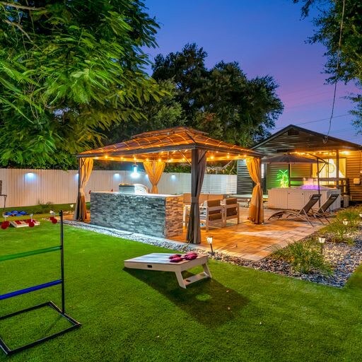 The property features an expansive backyard with a covered pavilion, outdoor seating, and a lawn area for games and relaxation under evening skies.