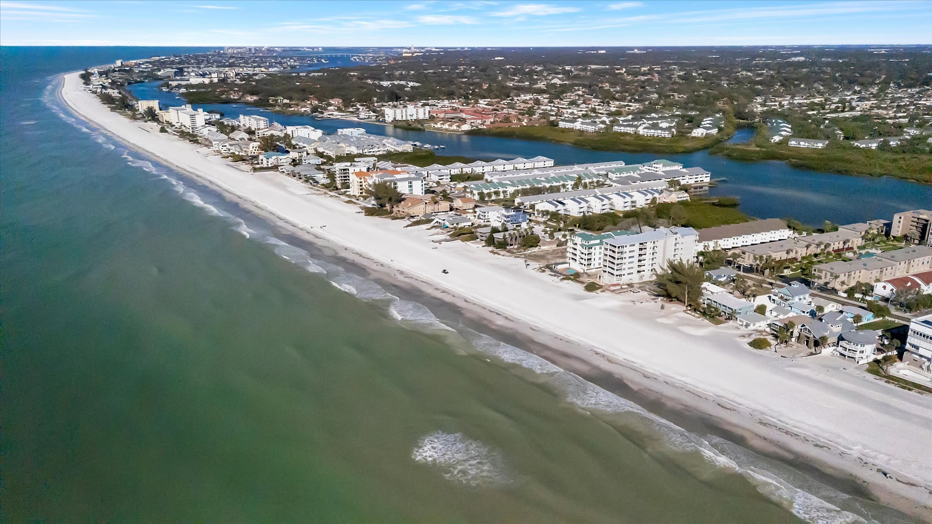 Aerial view of a stunning coastal community where pristine white-sand beaches meet calm turquoise waters, with scenic inlets and waterways nestled among residential neighborhoods.