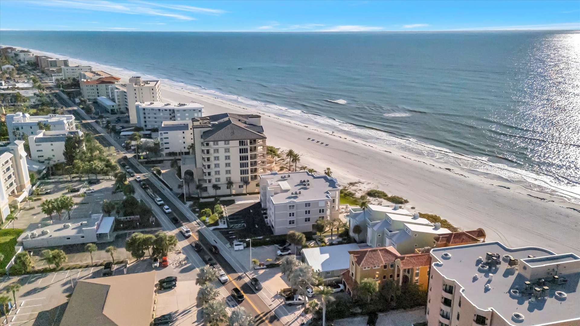 An aerial view capturing the property nestled along a pristine stretch of coastline, where gentle waves meet soft sand and the neighborhood offers convenient coastal living.