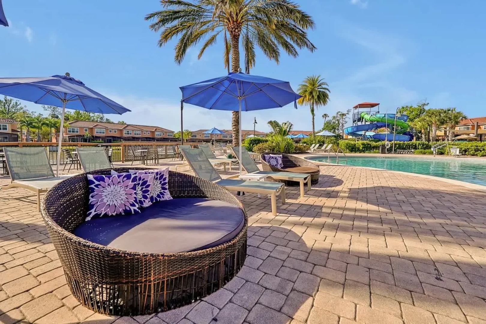Relax poolside on plush lounge chairs and luxurious daybeds, shaded by oversized umbrellas. Palm trees sway overhead while a fun water slide awaits in the background—your perfect escape.