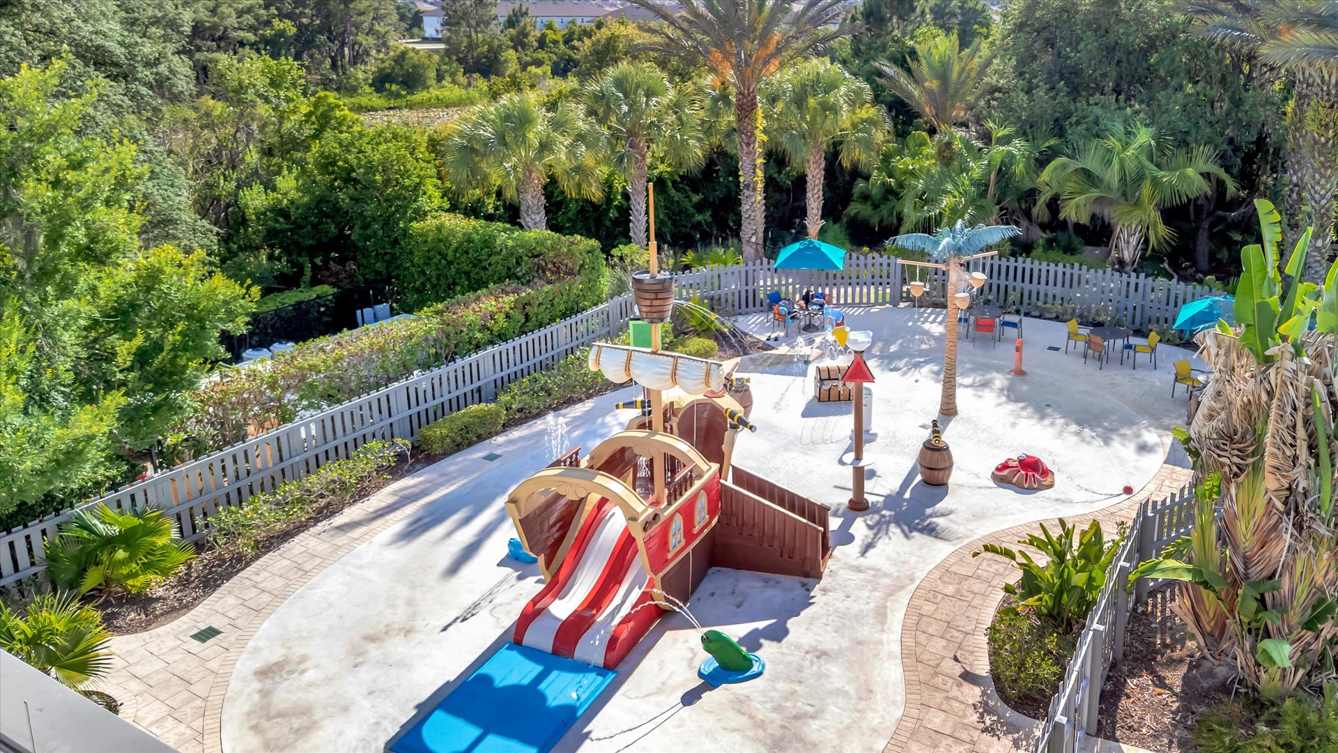 A nautical-themed playground featuring a vibrant pirate ship, palm trees, and colorful play structures set among lush tropical landscaping, providing a fun outdoor adventure for children.