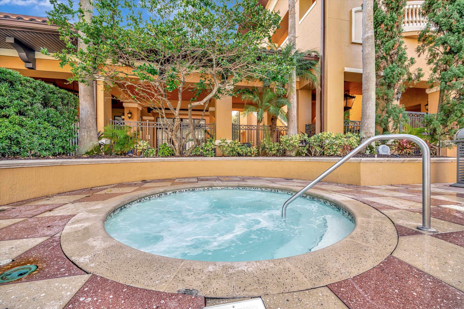 A welcoming hot tub nestled in a sunlit courtyard invites you to unwind after your day, surrounded by lush greenery and Mediterranean-style architecture.
