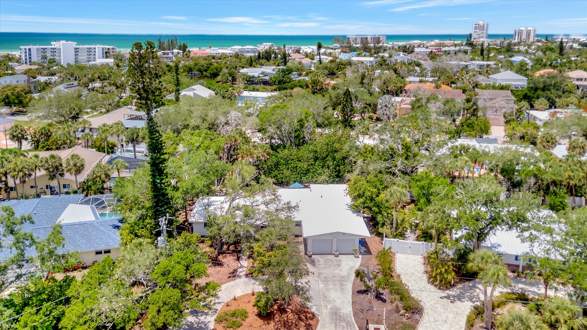 Aerial view of the property nestled in a lush, tree-lined neighborhood with turquoise waters visible in the distance—a peaceful coastal retreat awaits your arrival.