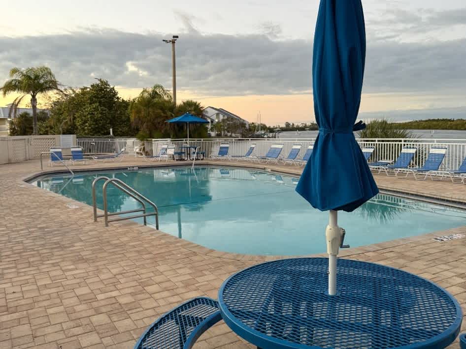 The pool area features tranquil waterfront views and vibrant Florida landscaping surrounding the community, with comfortable lounge seating and shaded umbrellas awaiting your arrival.