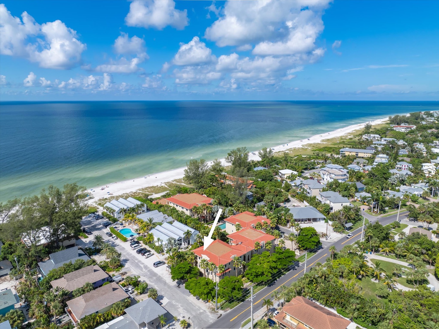 An aerial view captures the property's prime beachfront location on pristine white sand shores, nestled in a lush coastal neighborhood just steps from turquoise Gulf waters.