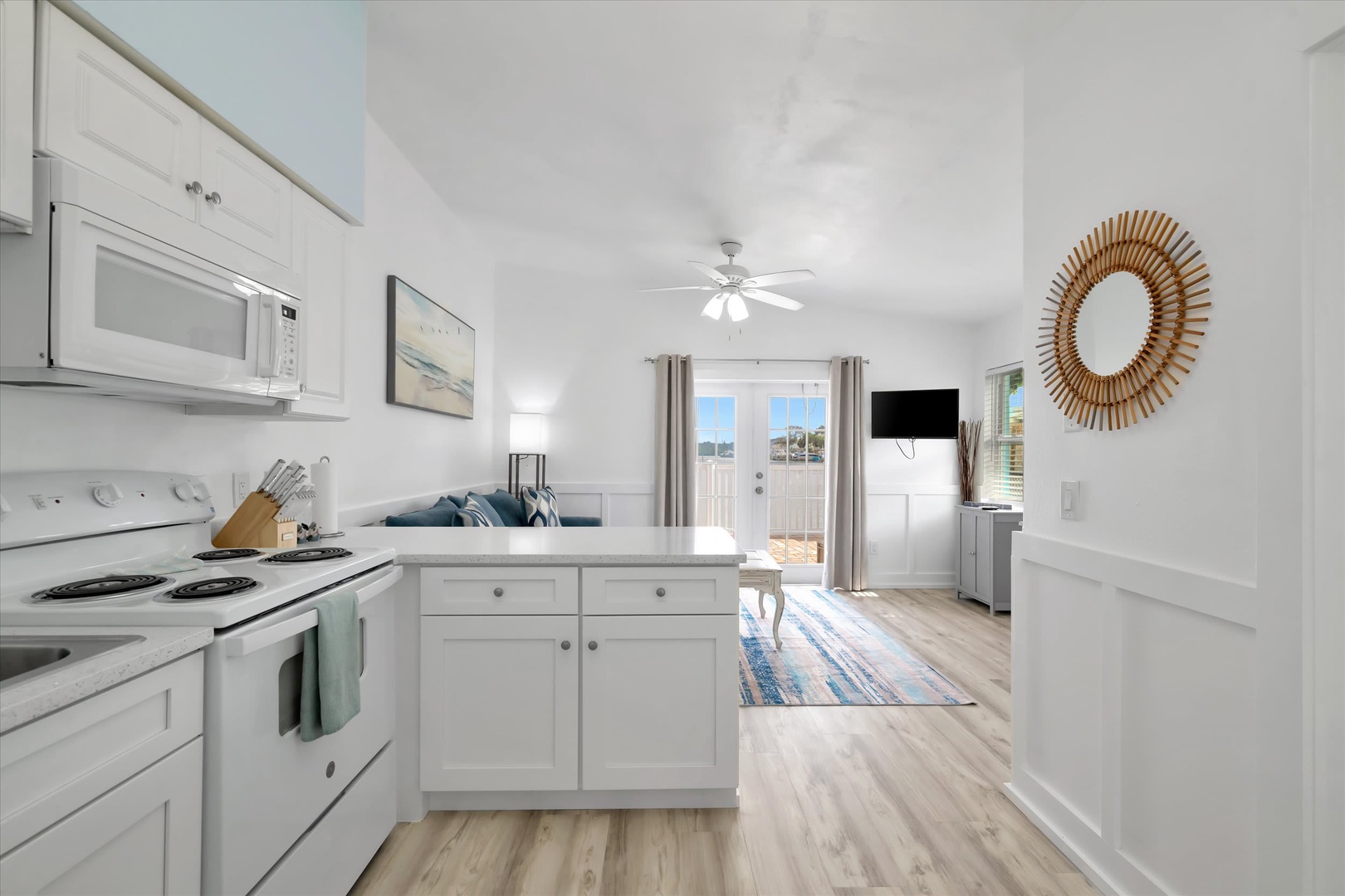 Step into your bright coastal retreat with a fully equipped kitchen, welcoming living space, and glimpses of the waterfront just beyond your door.