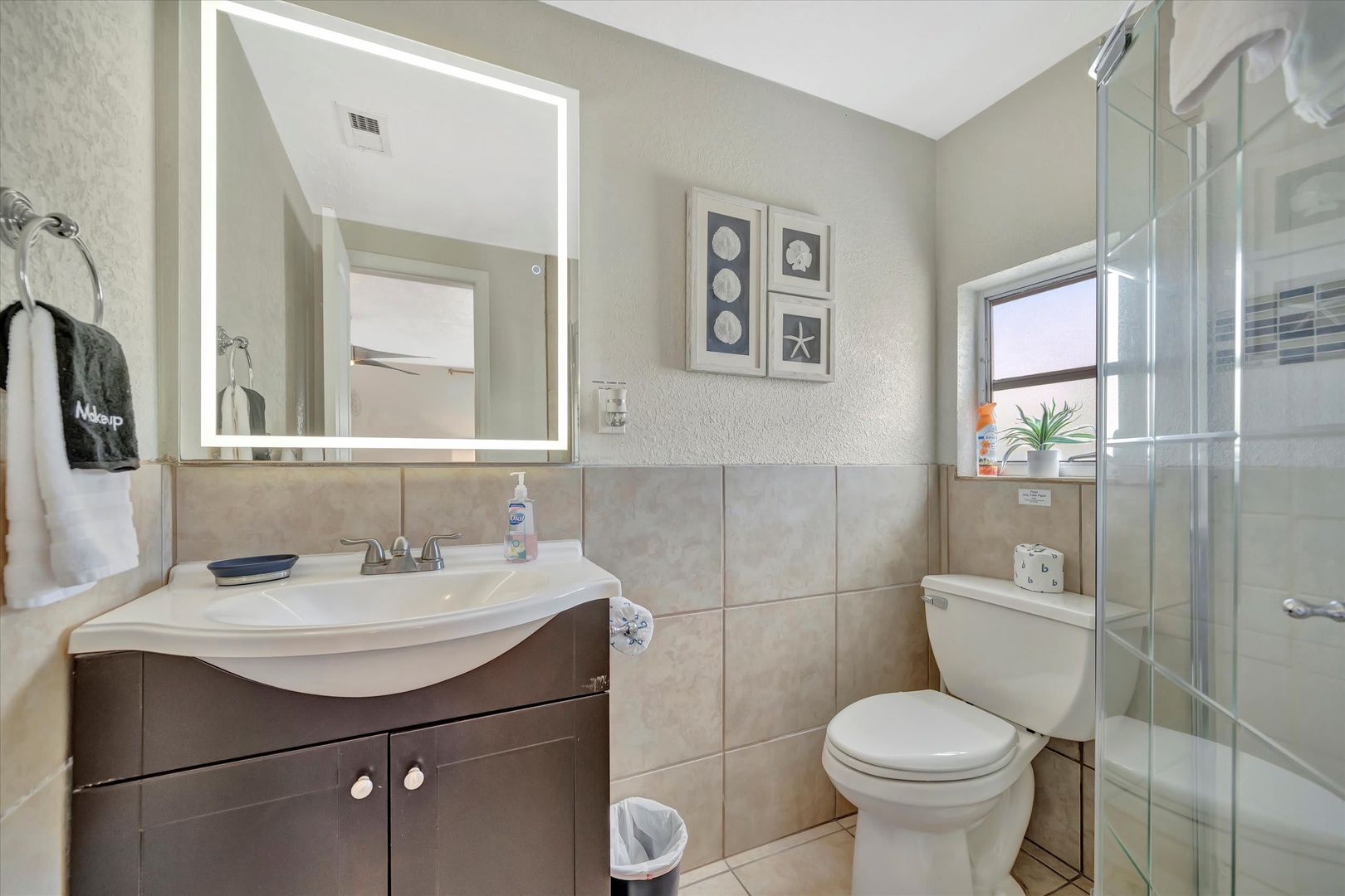 Your private bathroom offers a bright vanity with coastal-inspired décor, a sleek glass shower, and thoughtful touches like fresh towels to help you unwind after a day of exploring.