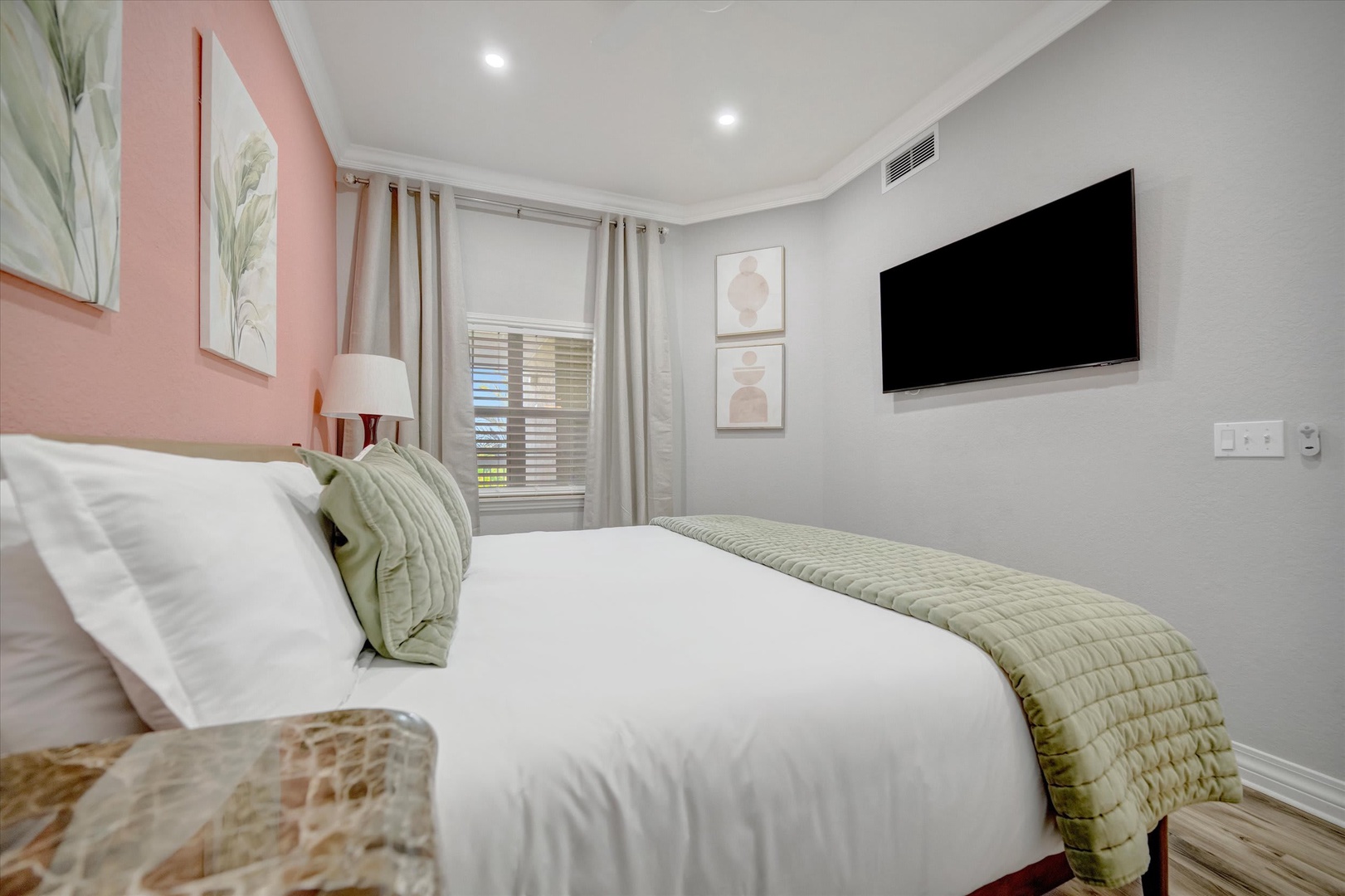 Slip into crisp white linens in your serene bedroom, where soft pink accents and natural light create the perfect retreat. Unwind with your favorite shows on the wall-mounted TV after a full day exploring.