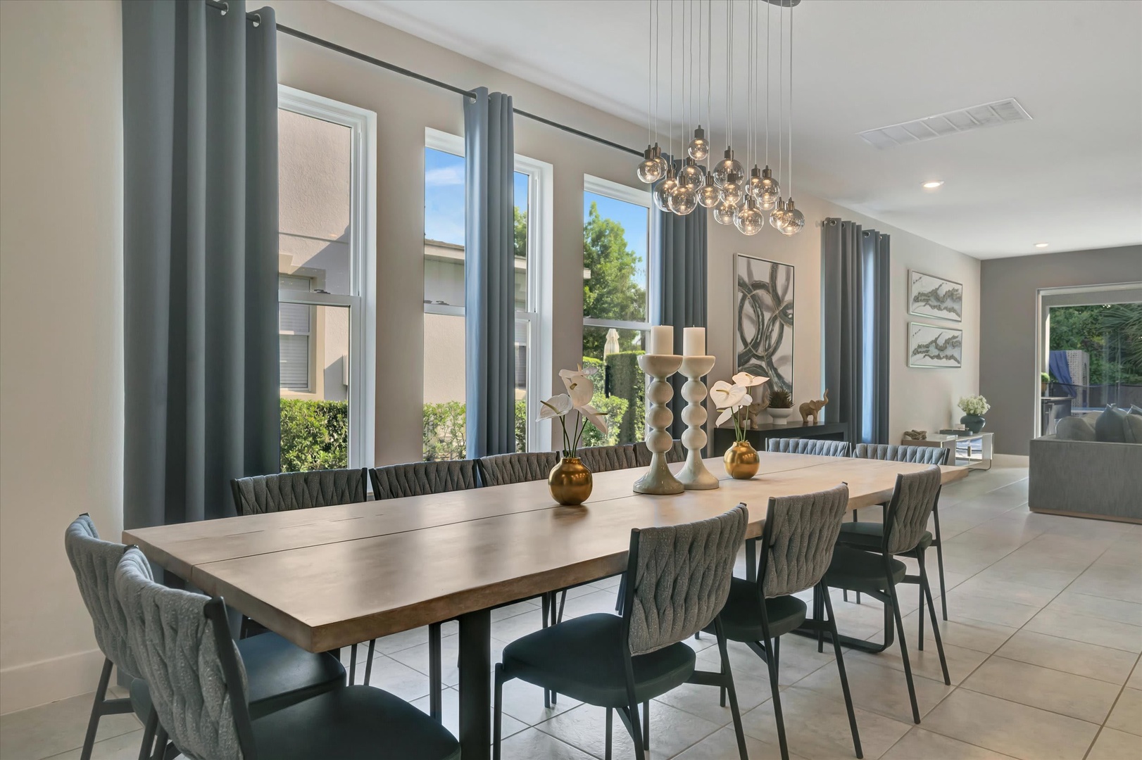 Gather around this elegant dining table for memorable meals together, with natural light streaming through tall windows and a stunning chandelier casting a warm glow overhead.