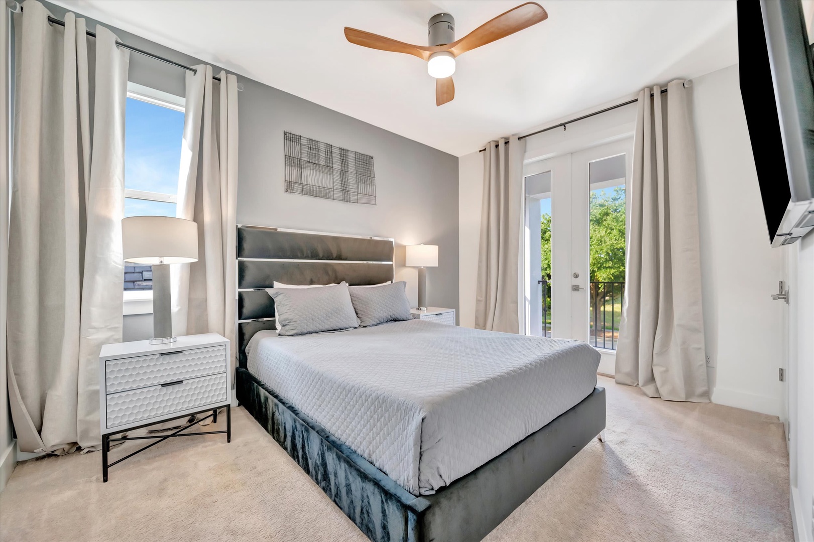 Your serene retreat awaits with a plush bed, gentle ceiling fan, and doors opening to lush greenery—rest easy in this bright, modern bedroom.