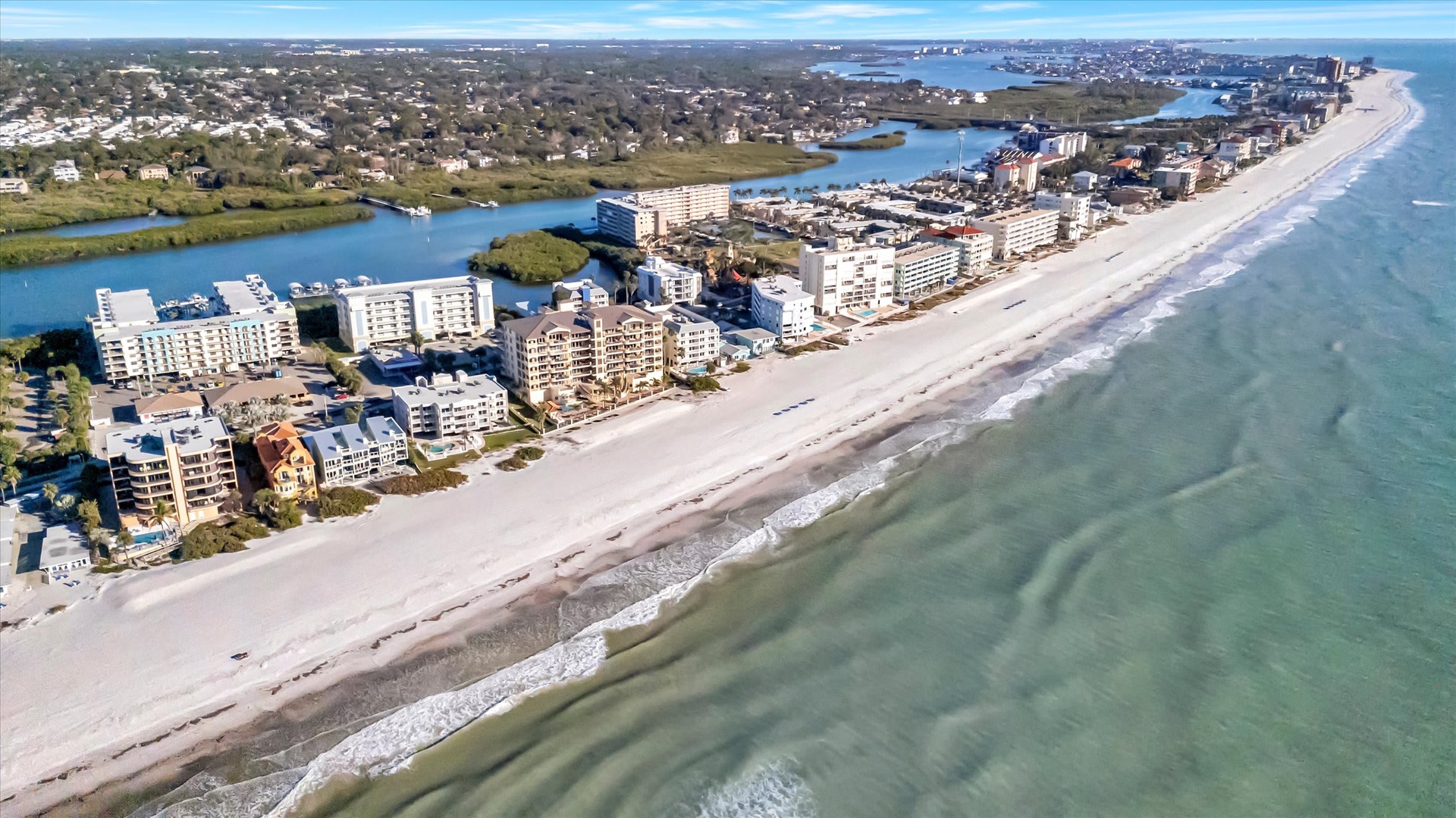 Aerial view of a coastal beachfront community, showcasing pristine sandy shores, nearby waterways, and surrounding neighborhoods.