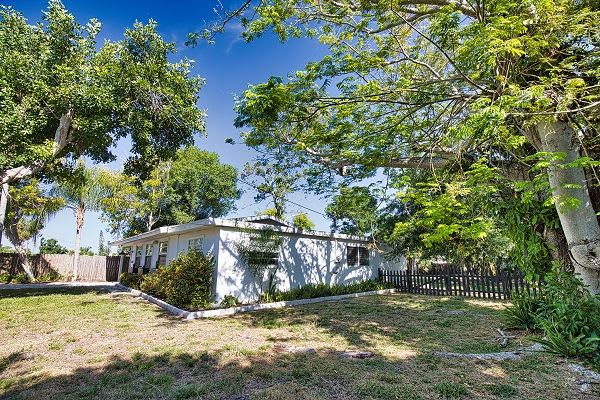 A charming vacation home nestled among lush tropical trees and greenery, offering a peaceful retreat in a sunny, tree-lined neighborhood.